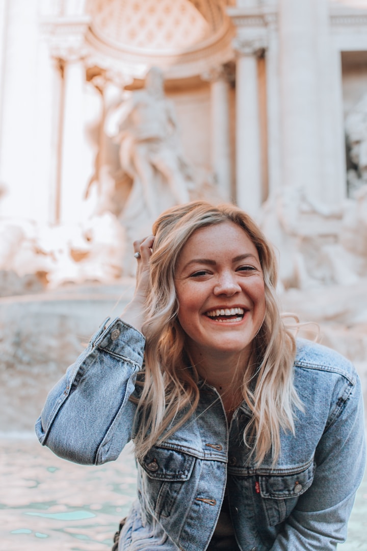 Giovane donna sorridente in primo piano, davanti a una fontana storica.