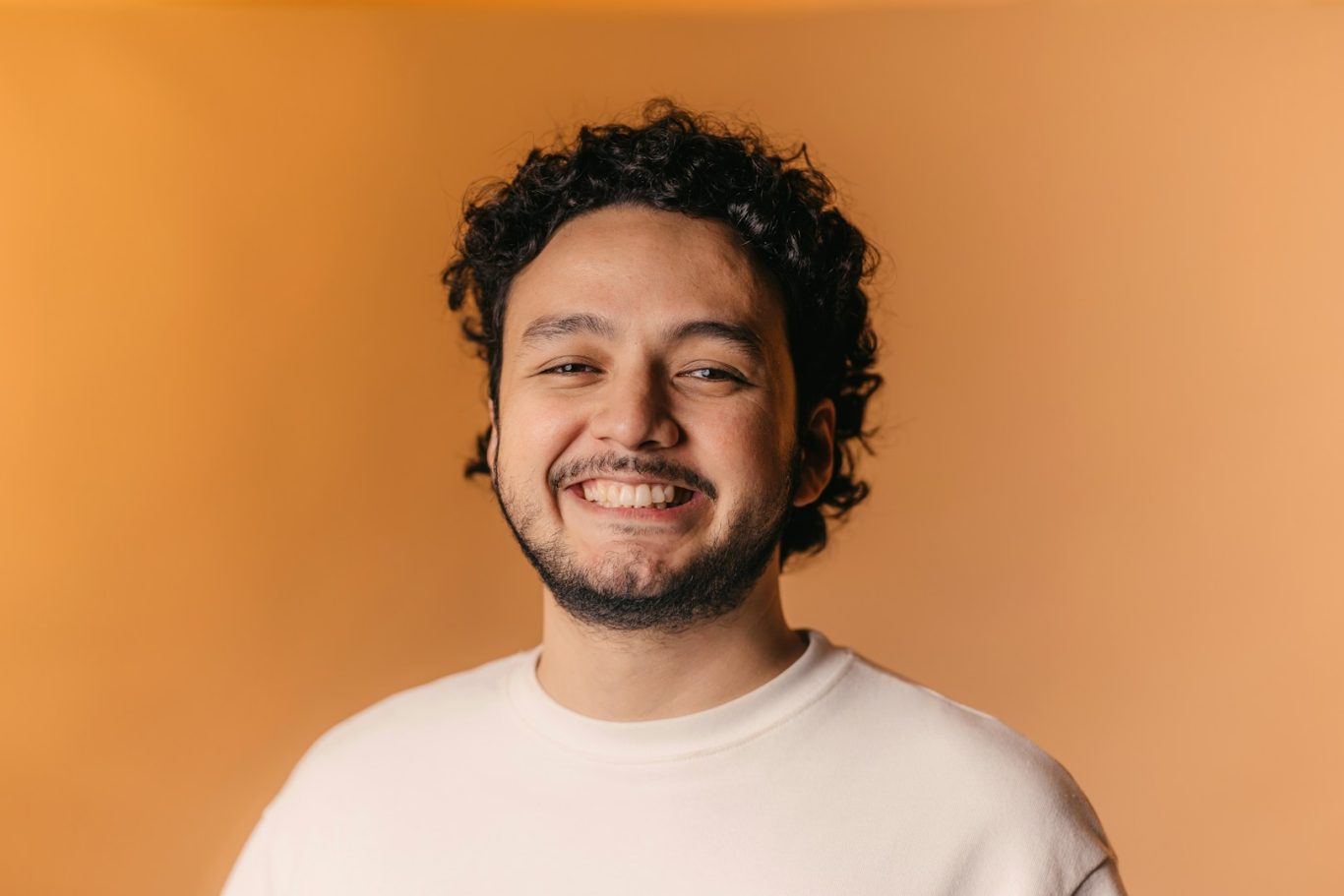 Uomo sorridente con capelli ricci su sfondo arancione.