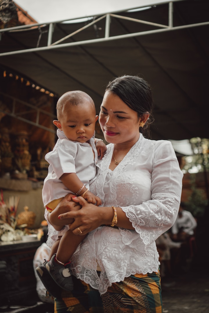Donna in abito tradizionale tiene in braccio un bambino che indossa una camicia bianca.