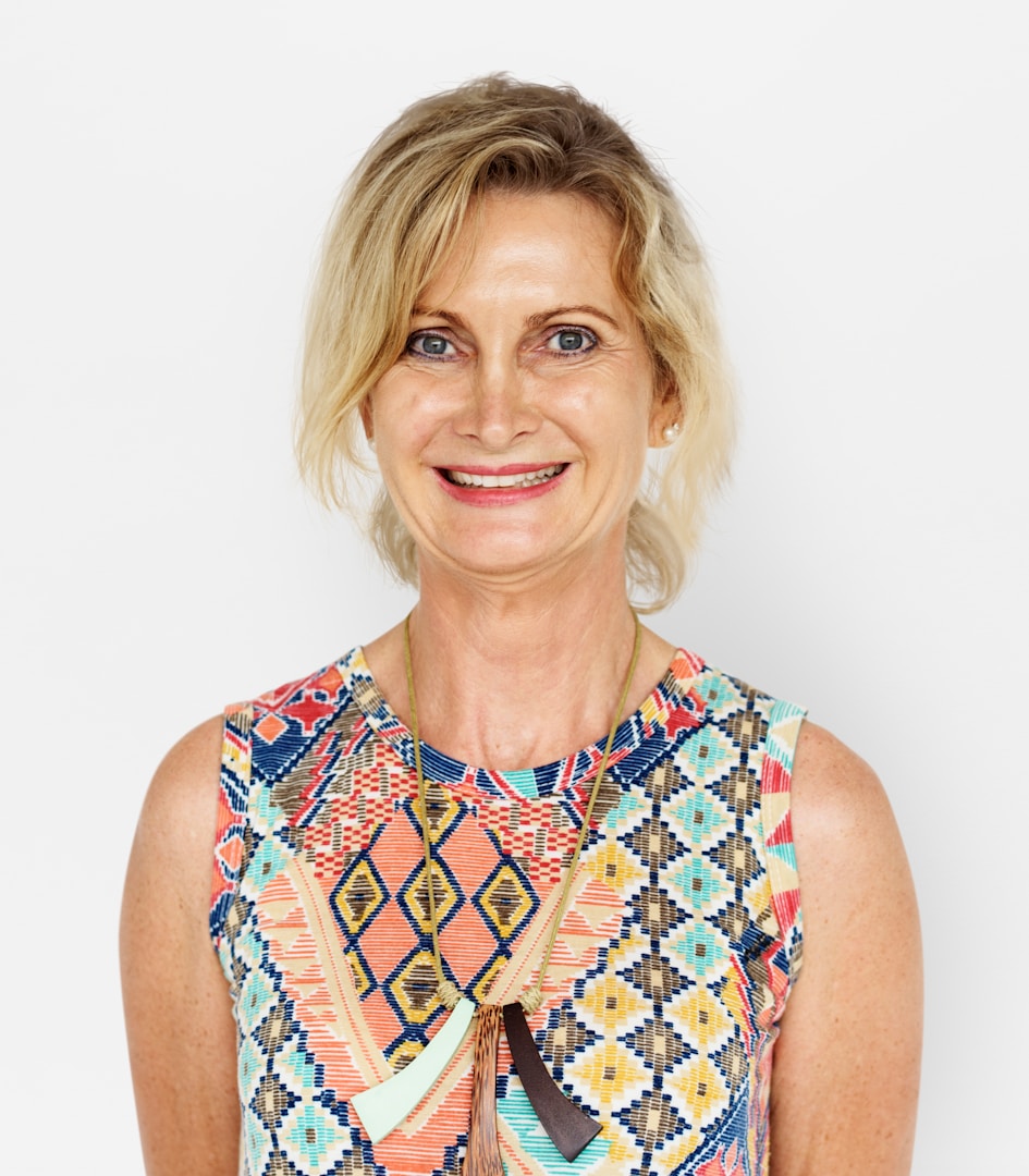 Donna con capelli biondi e un vestito colorato, sorride alla fotocamera.